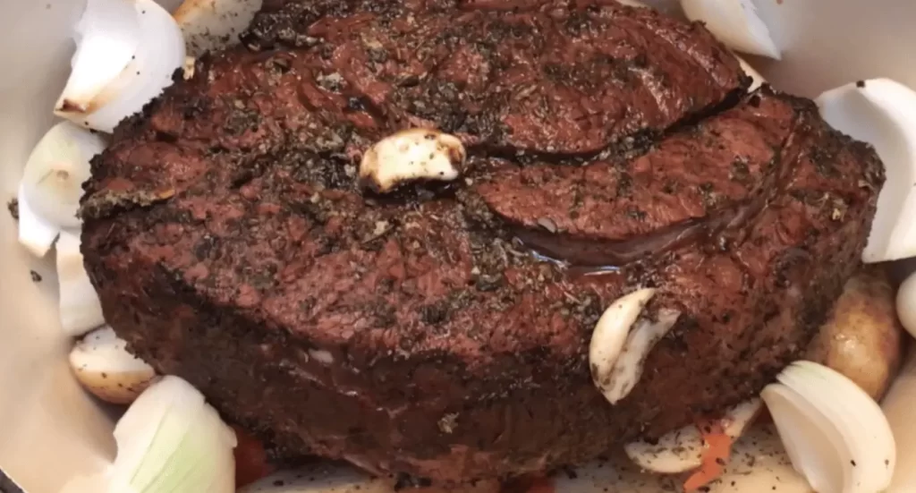 Raw beef chuck roast seasoned with salt, pepper, and herbs.