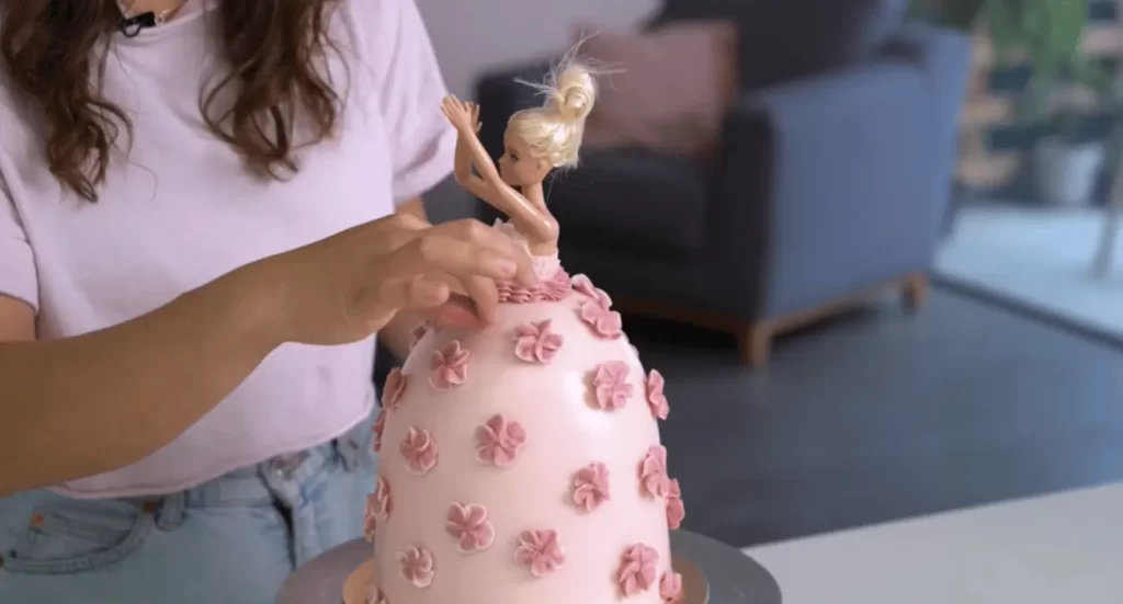 Barbie cake with a pink fondant dress and elegant decorations on a cake stand.