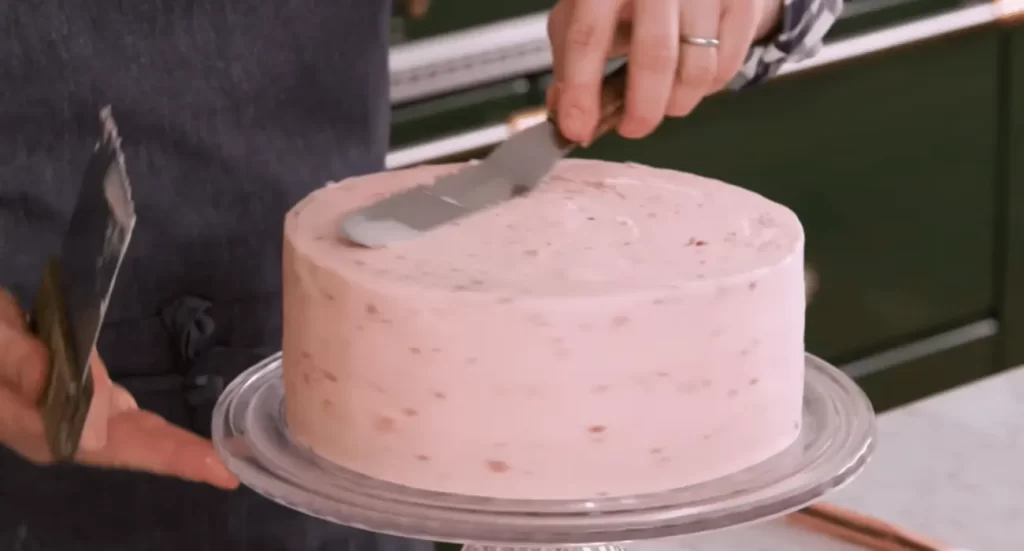 A person cutting into a strawberry chocolate cake, revealing layers of chocolate and strawberry filling.