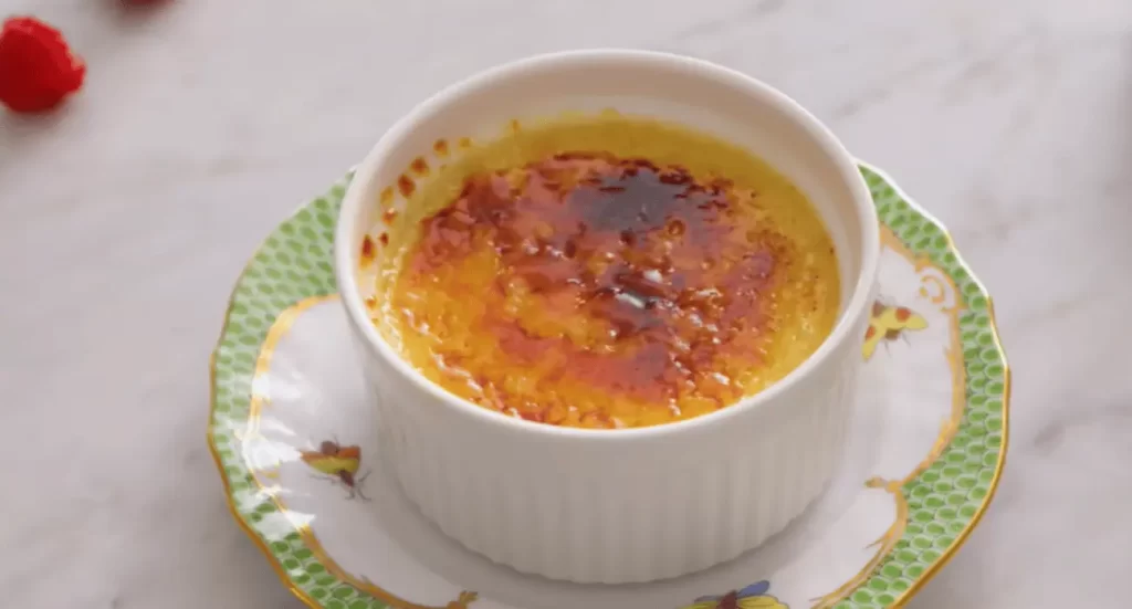 Close-up of a gourmet crab brulee with a golden caramelized sugar topping and garnished with fresh herbs.