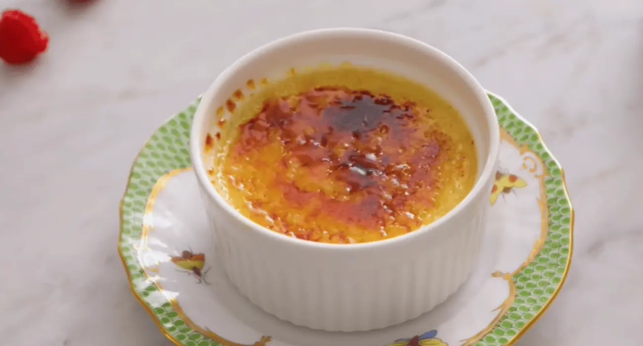 Close-up of a gourmet crab brulee with a golden caramelized sugar topping and garnished with fresh herbs.