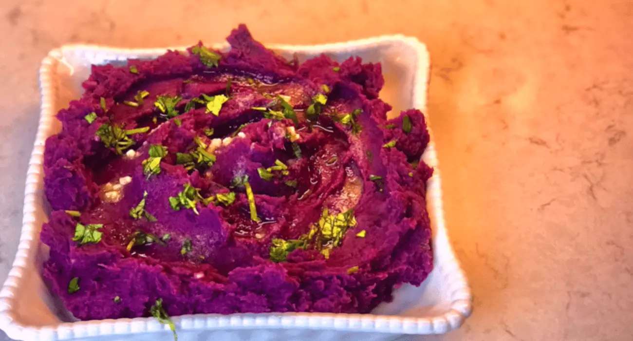 Close-up of a purple sweet potato pie slice with a golden-brown crust, topped with a dollop of whipped cream on a white plate