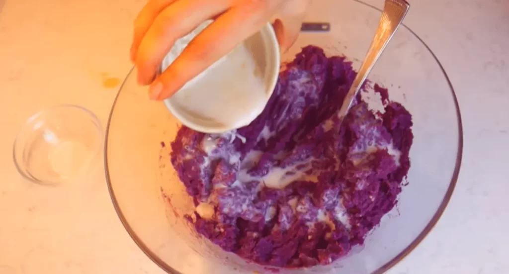 Bowl of creamy purple sweet potato smoothie topped with granola, sliced bananas, and chia seeds, set against a pastel background