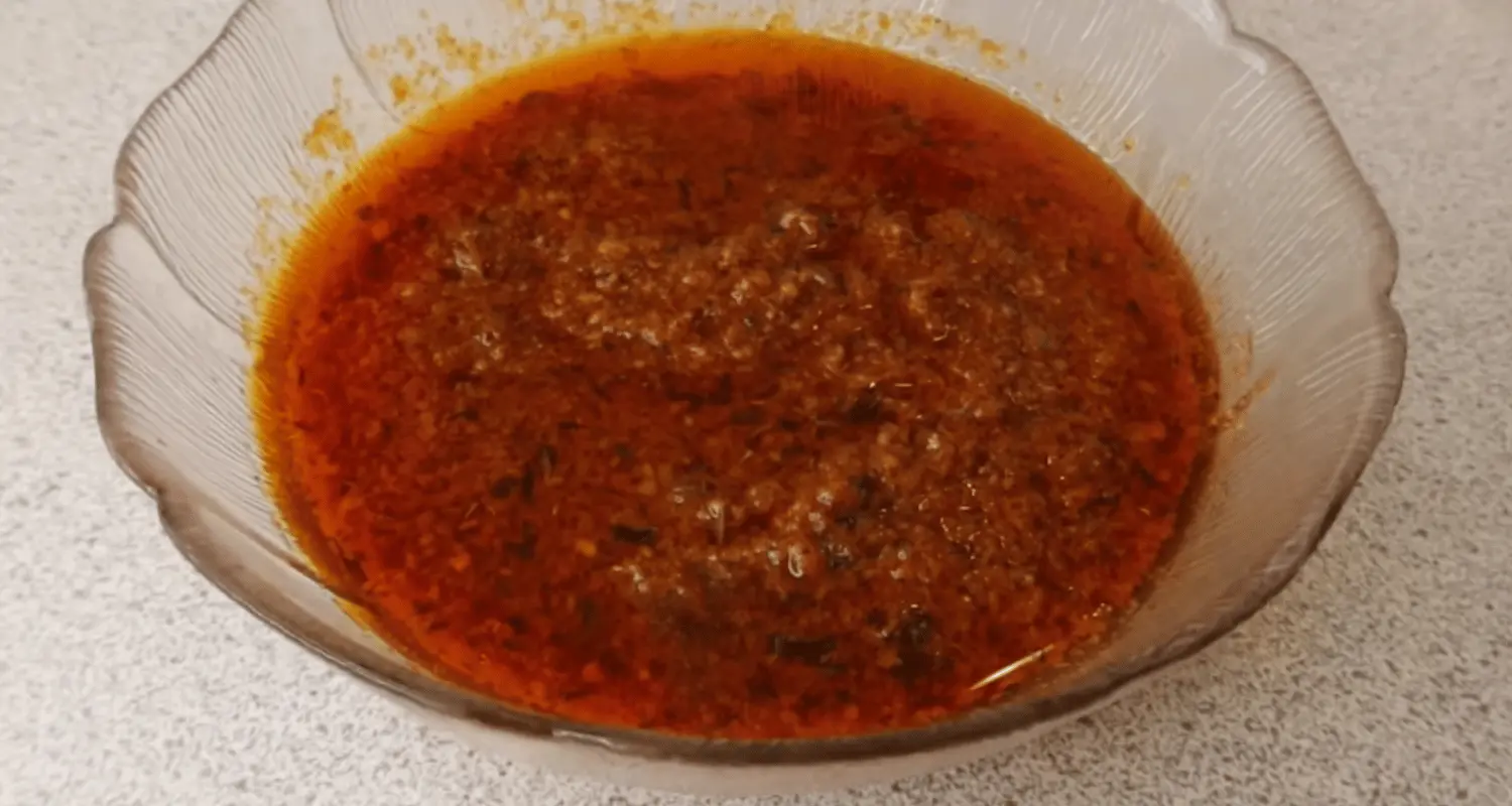 Close-up of a bowl of spicy seafood boil sauce with fresh herbs and lemon slices, alongside a variety of seafood such as shrimp, crab, and clams